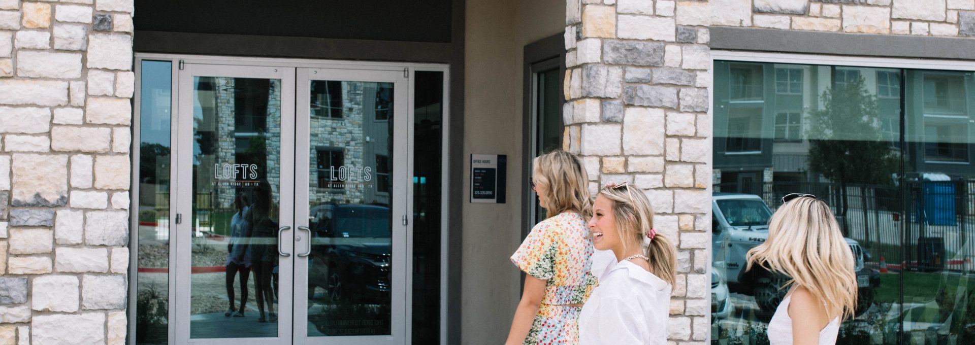 three women walking out of a building with a sign that says, welcome to the new apartment at The Lofts at Allen Ridge