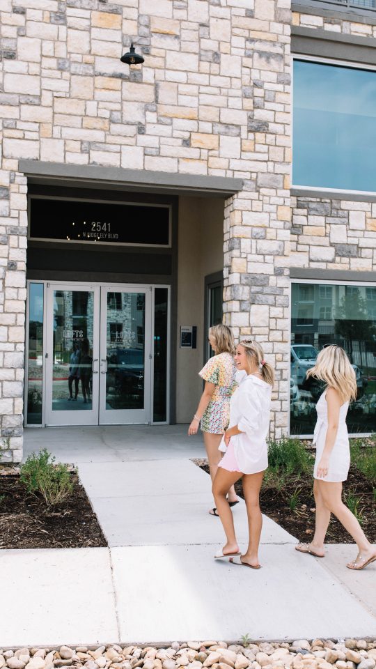 three women walking out of a building with a sign that says, welcome to the new apartment at The Lofts at Allen Ridge