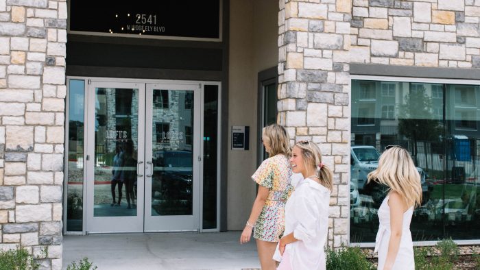 three women walking out of a building with a sign that says, welcome to the new apartment at The Lofts at Allen Ridge